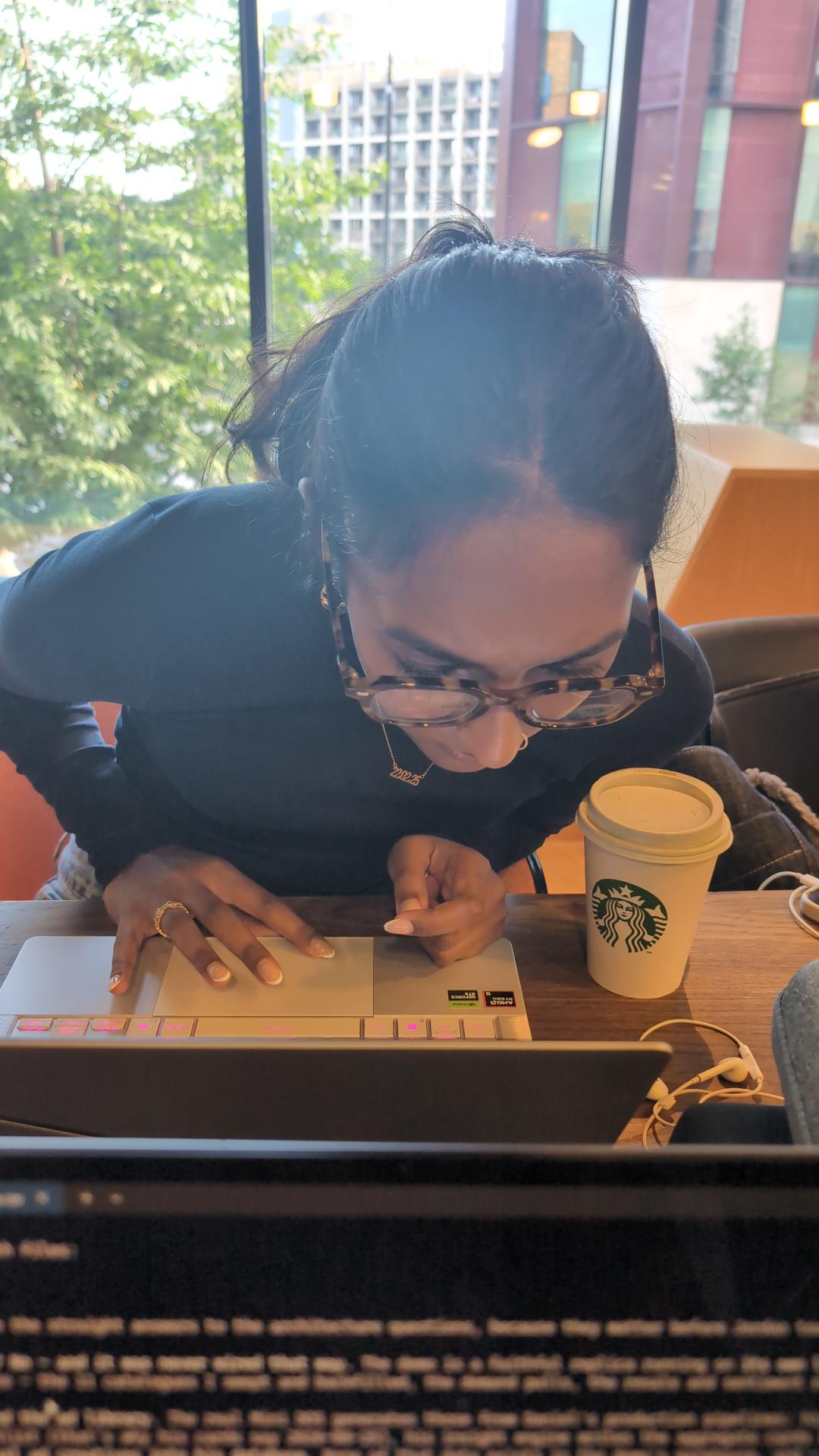 Kaysh working on a laptop by a window with a coffee cup