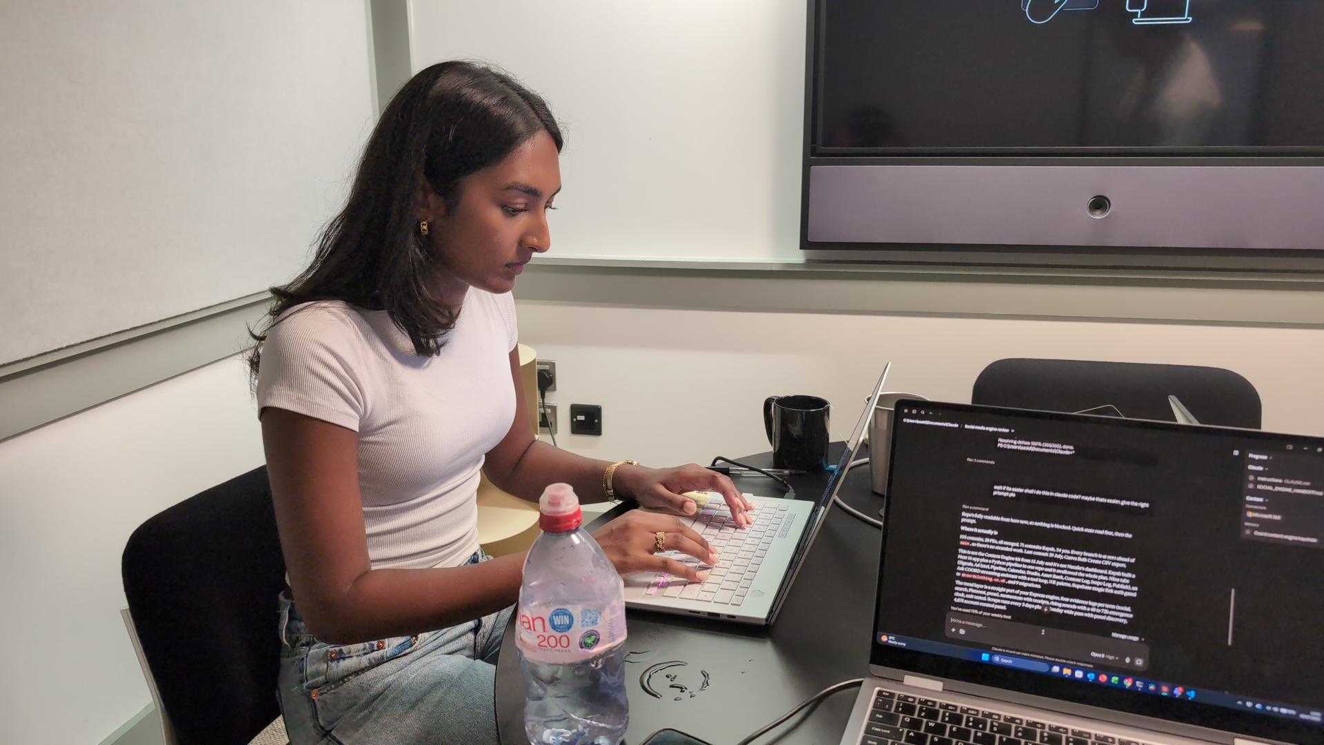 Kaysh typing on a laptop in a meeting room with code on screen